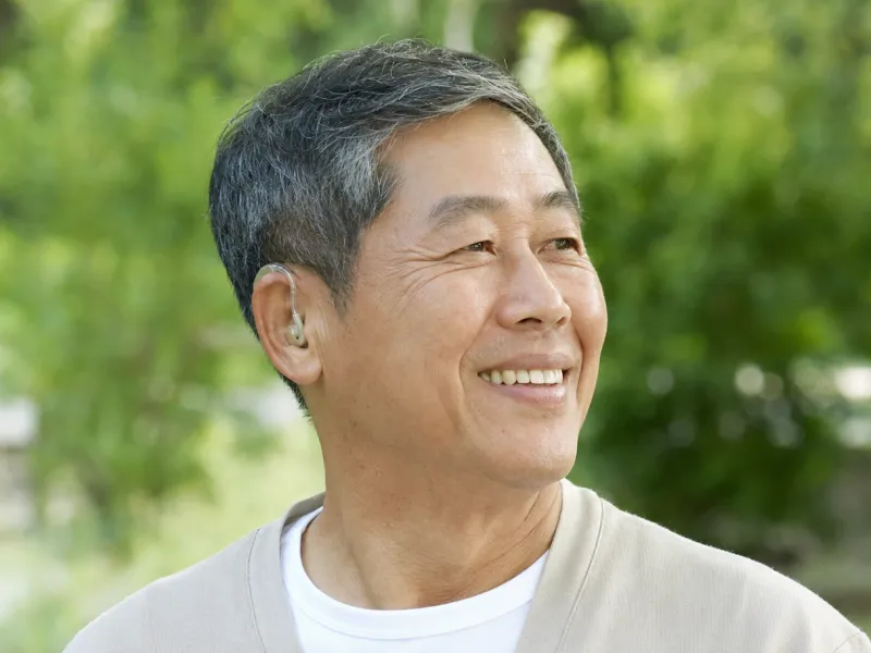 보청기를 착용한 노인이 야외에서 밝게 미소짓는 모습